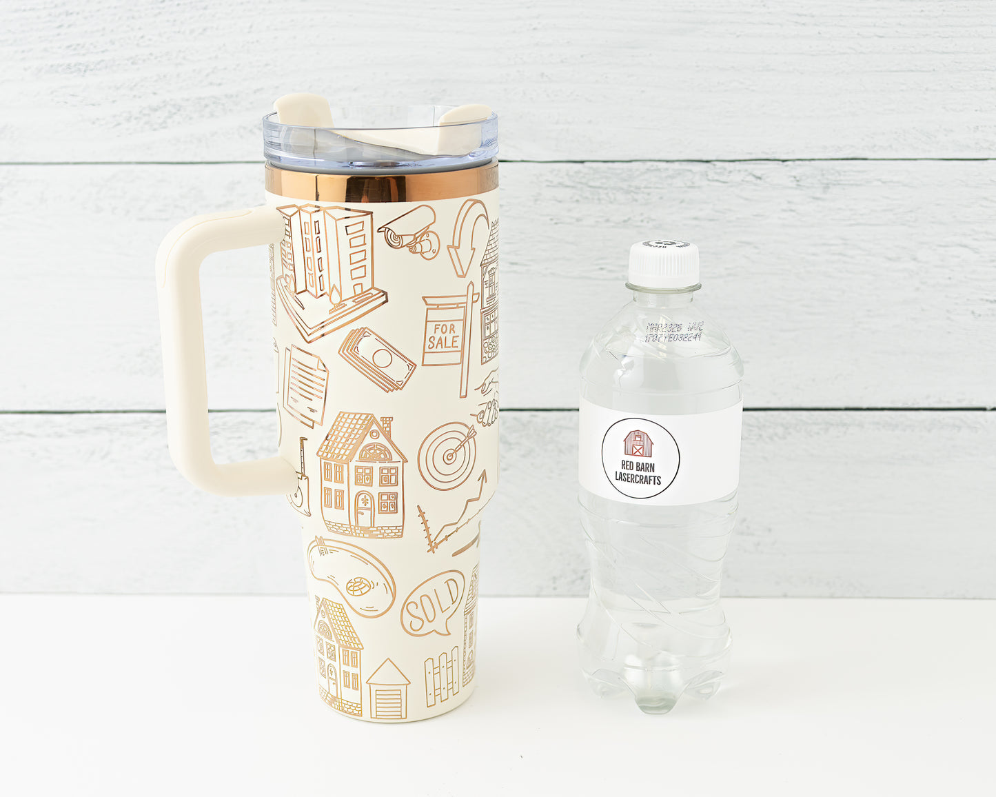 Tumbler with real estate-themed design on a wood background shown with water bottle for size comparison.