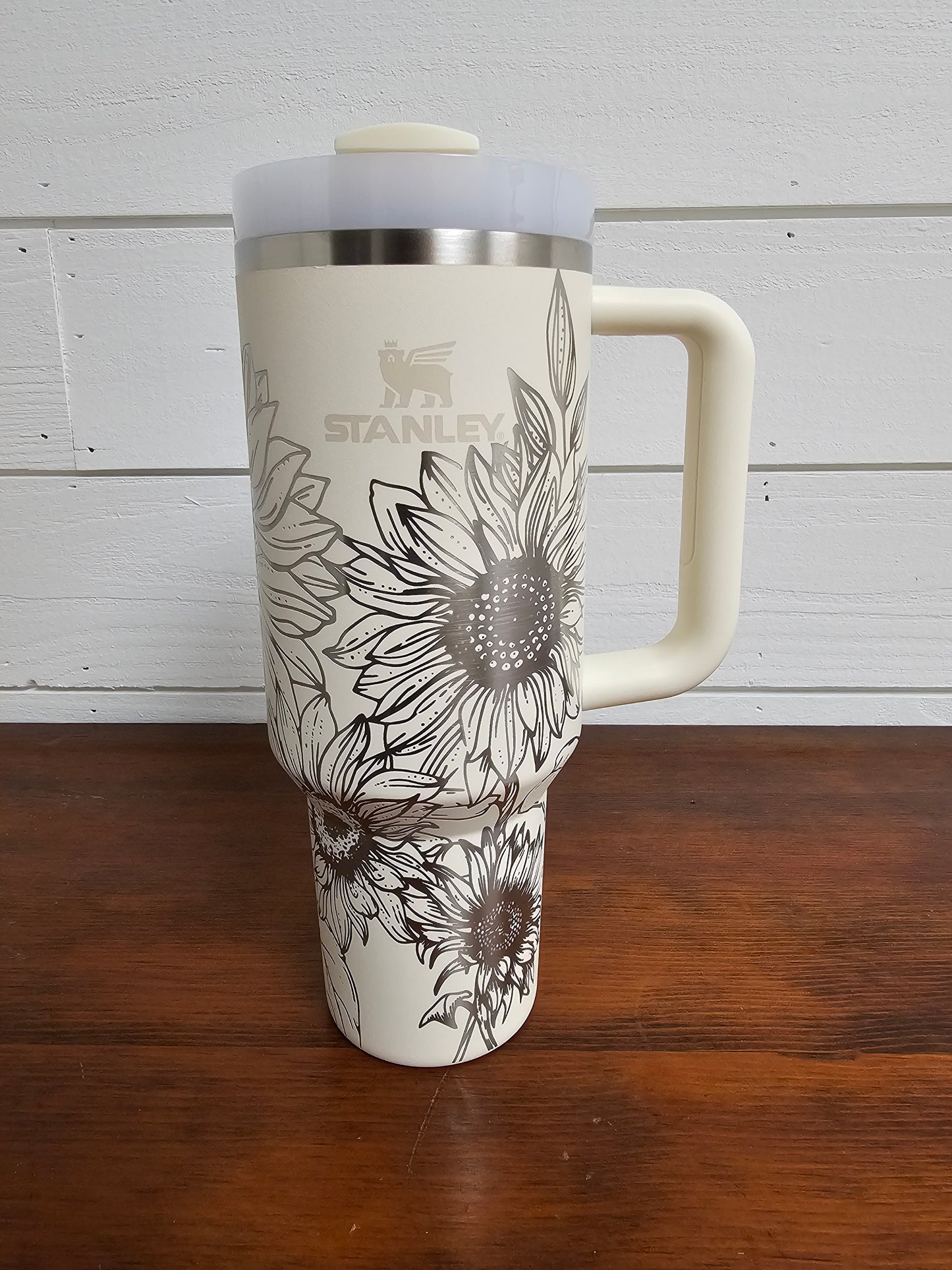 Sunflower wrap laser engraved 40oz cream Stanley tumbler displayed on a wooden table with a white shiplap background
