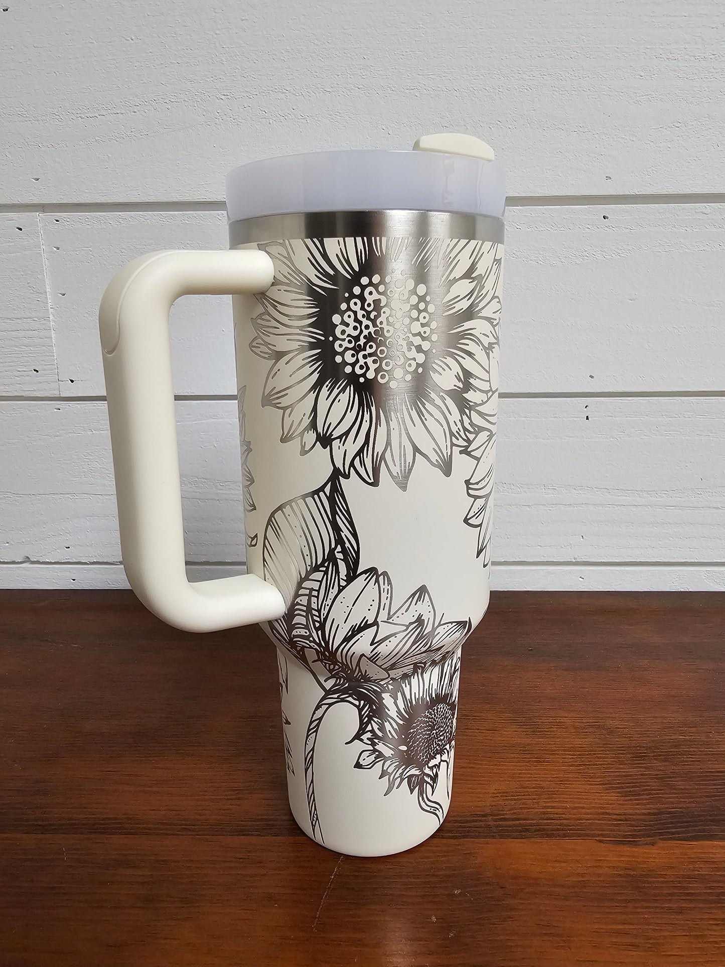 Sunflower wrap laser engraved 40oz cream Stanley tumbler displayed on a wooden table with a white shiplap background