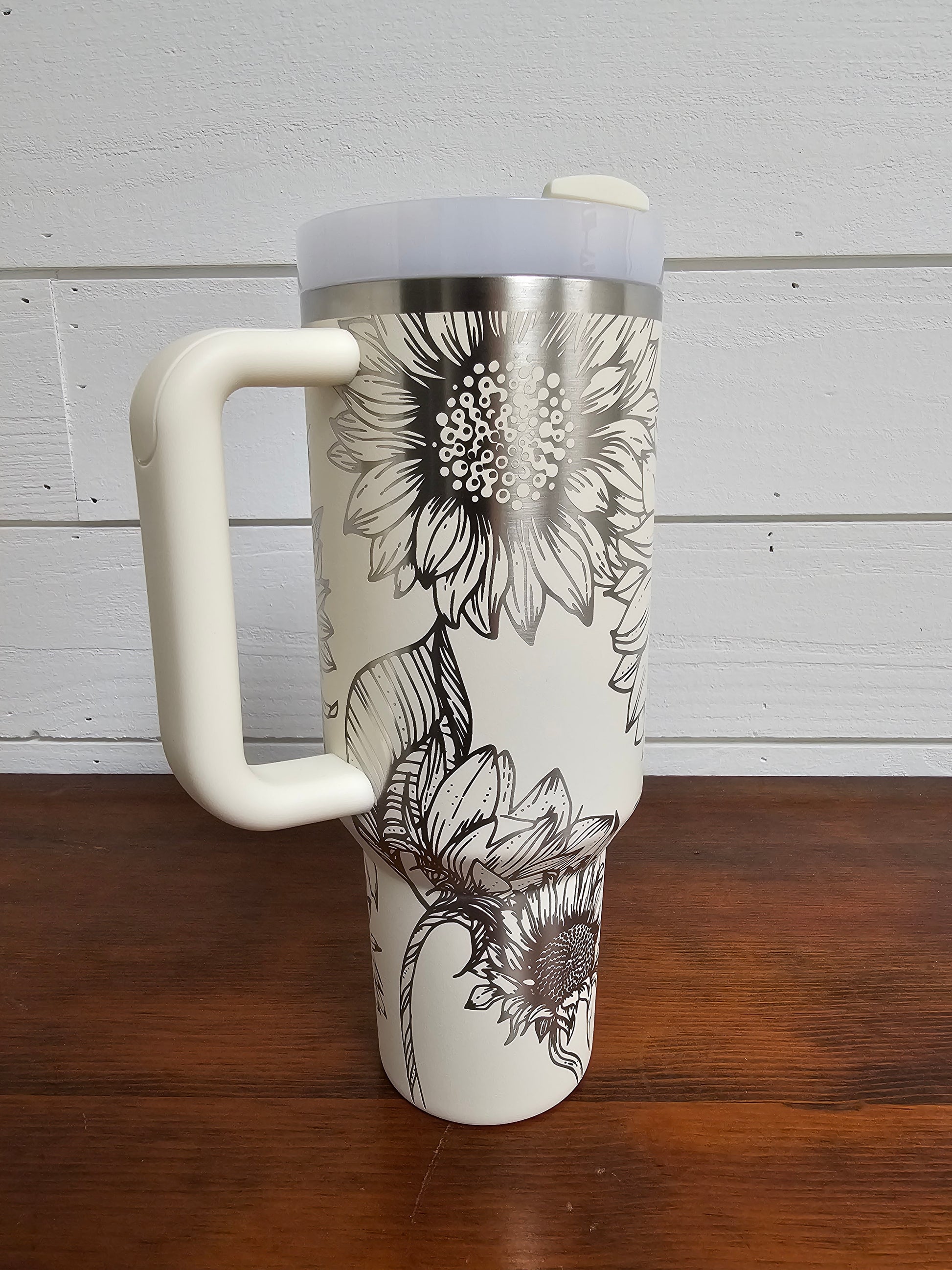 Sunflower wrap laser engraved 40oz cream Stanley tumbler displayed on a wooden table with a white shiplap background