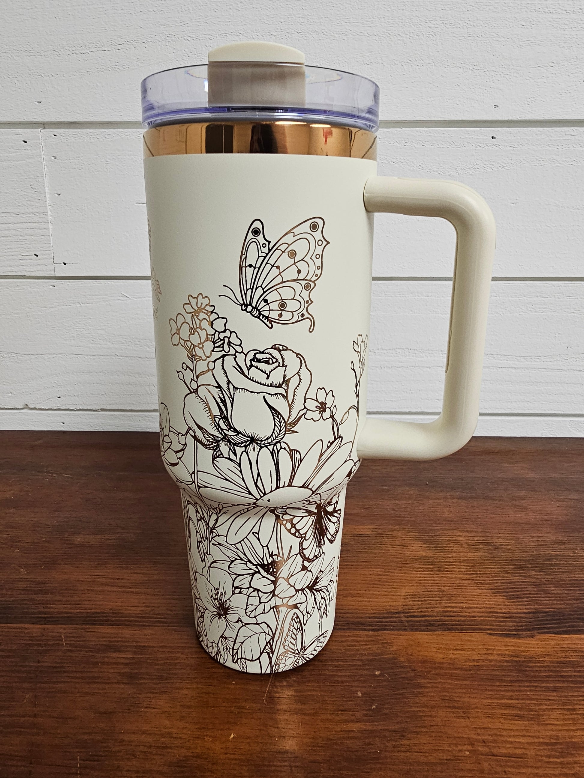 Cream and copper tumbler with floral and butterfly design on a white shiplap background