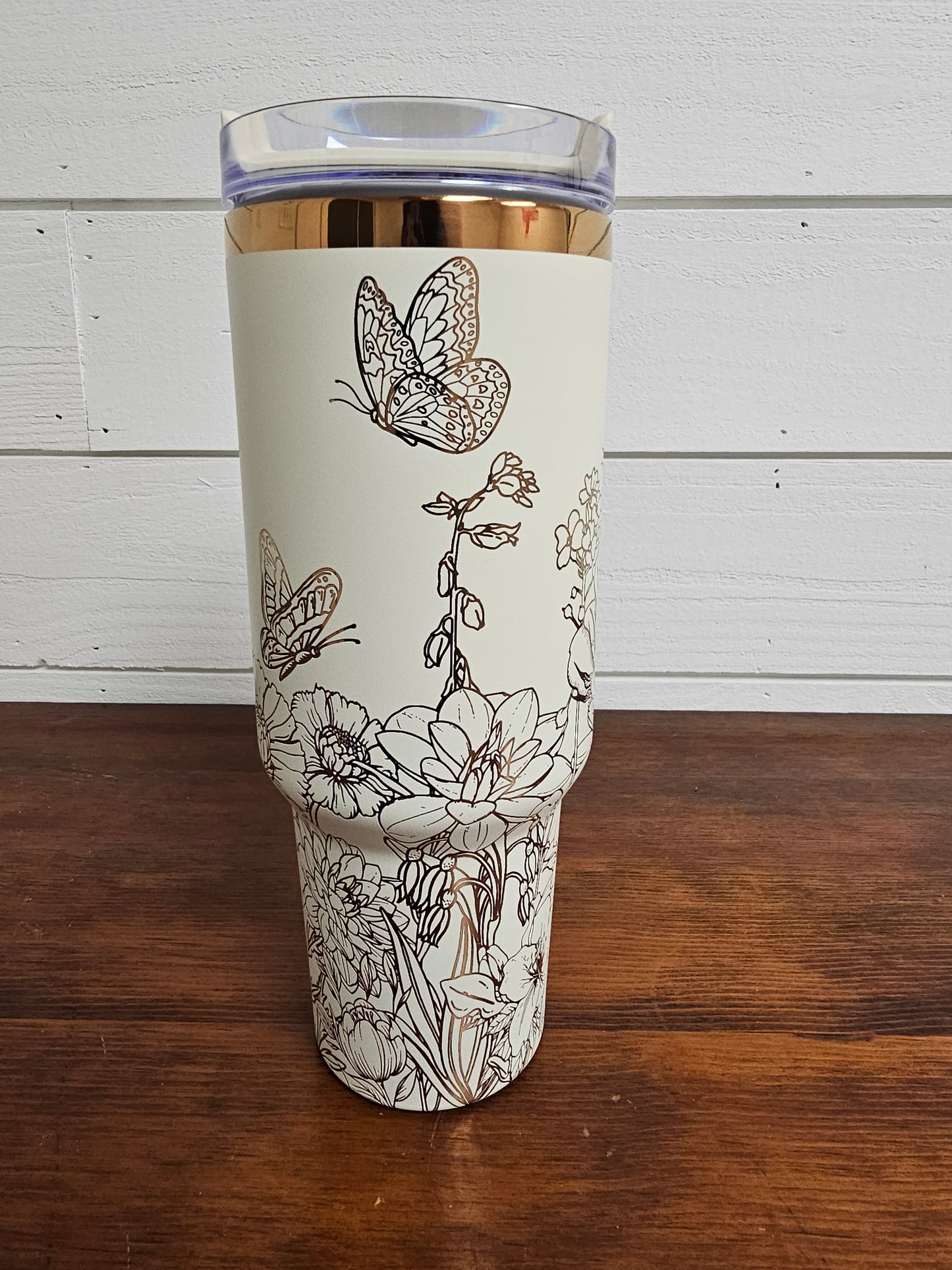 Cream and copper tumbler with floral and butterfly design on a white shiplap background