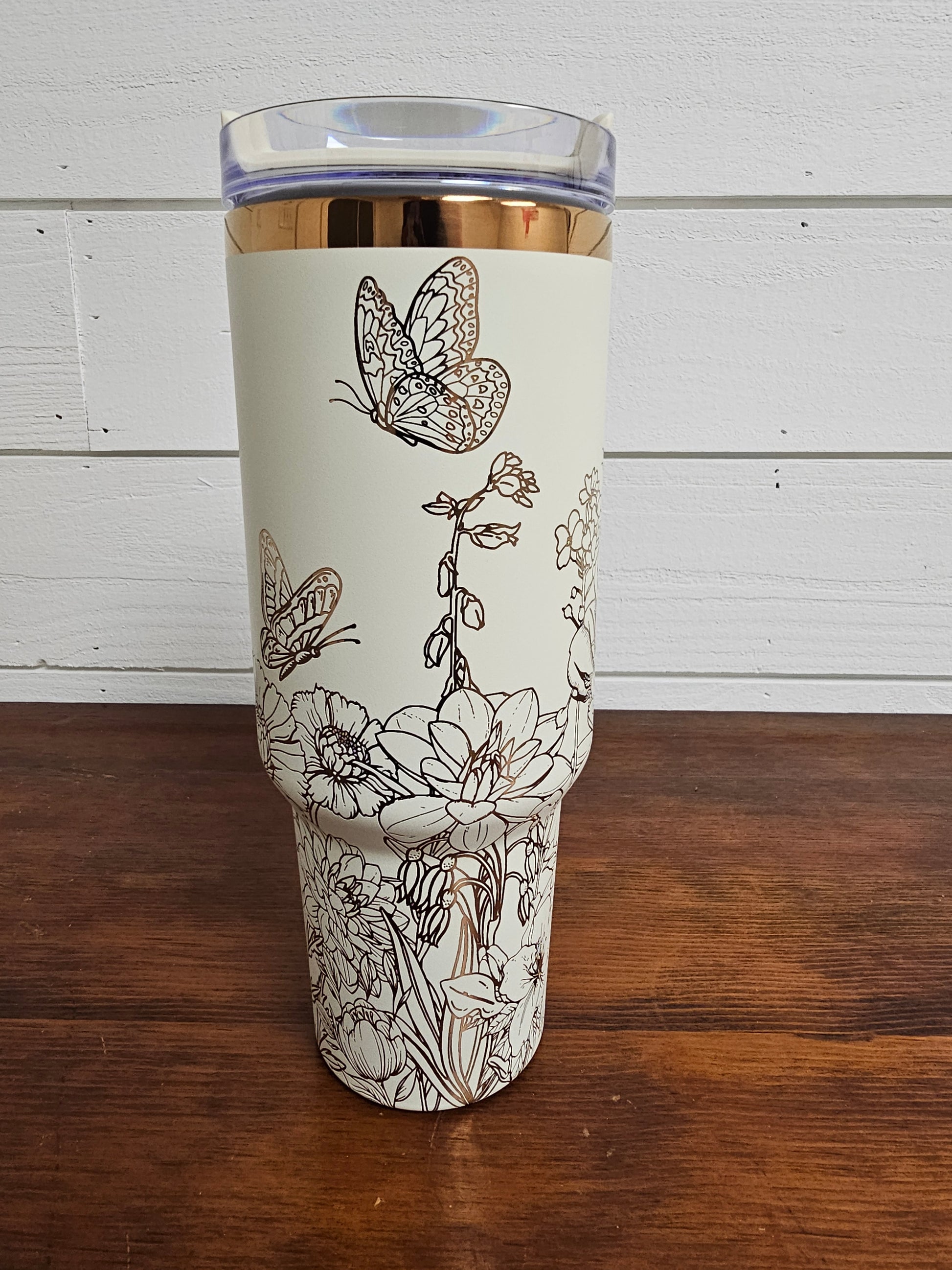 Cream and copper tumbler with floral and butterfly design on a white shiplap background