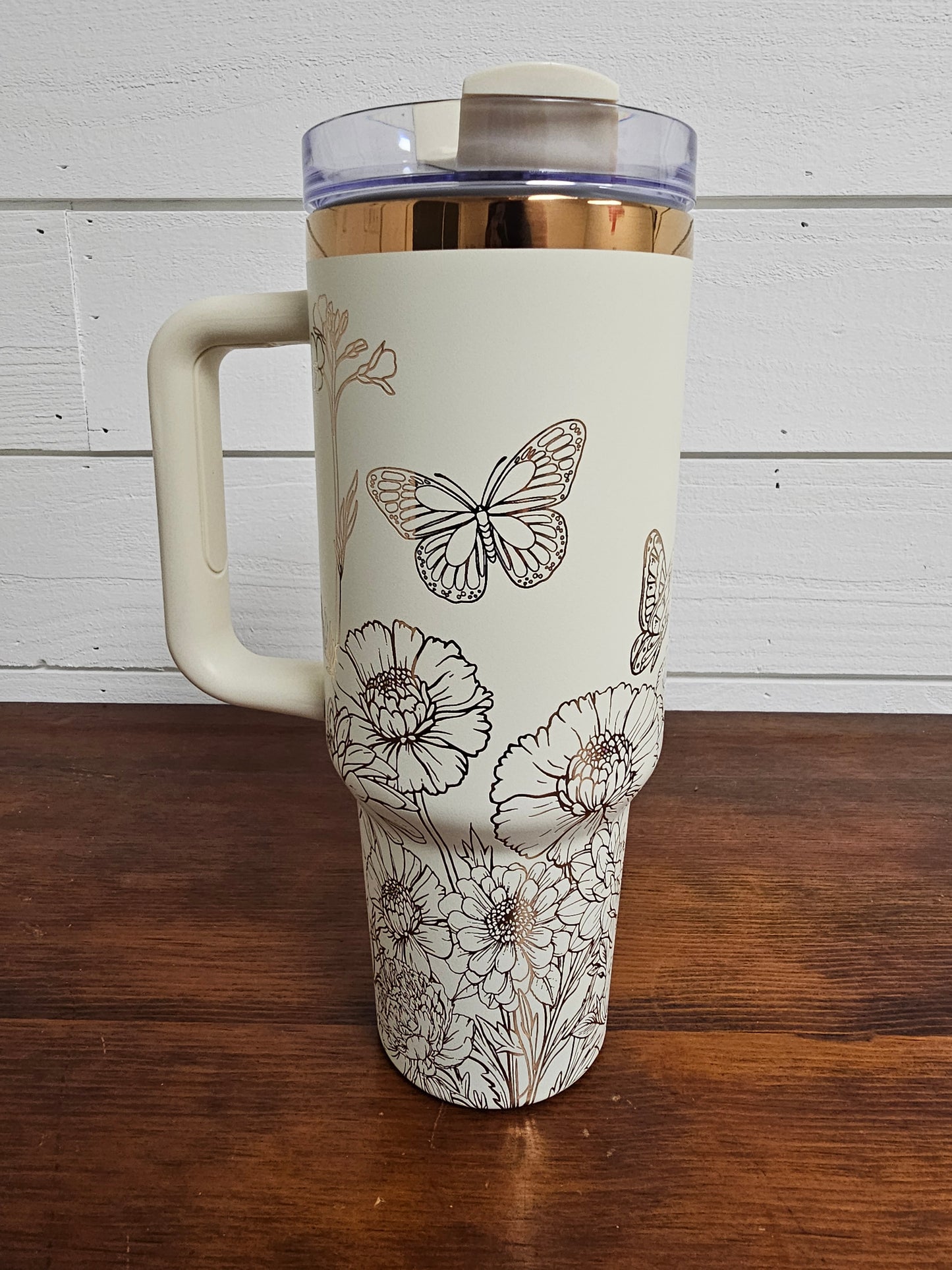 Cream and copper tumbler with floral and butterfly design on a white shiplap background