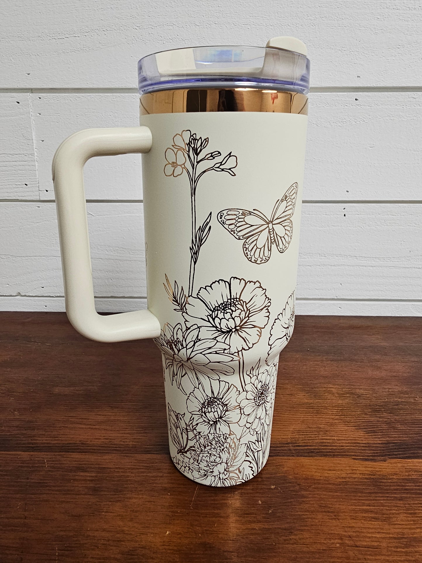 Cream and copper tumbler with floral and butterfly design on a white shiplap background