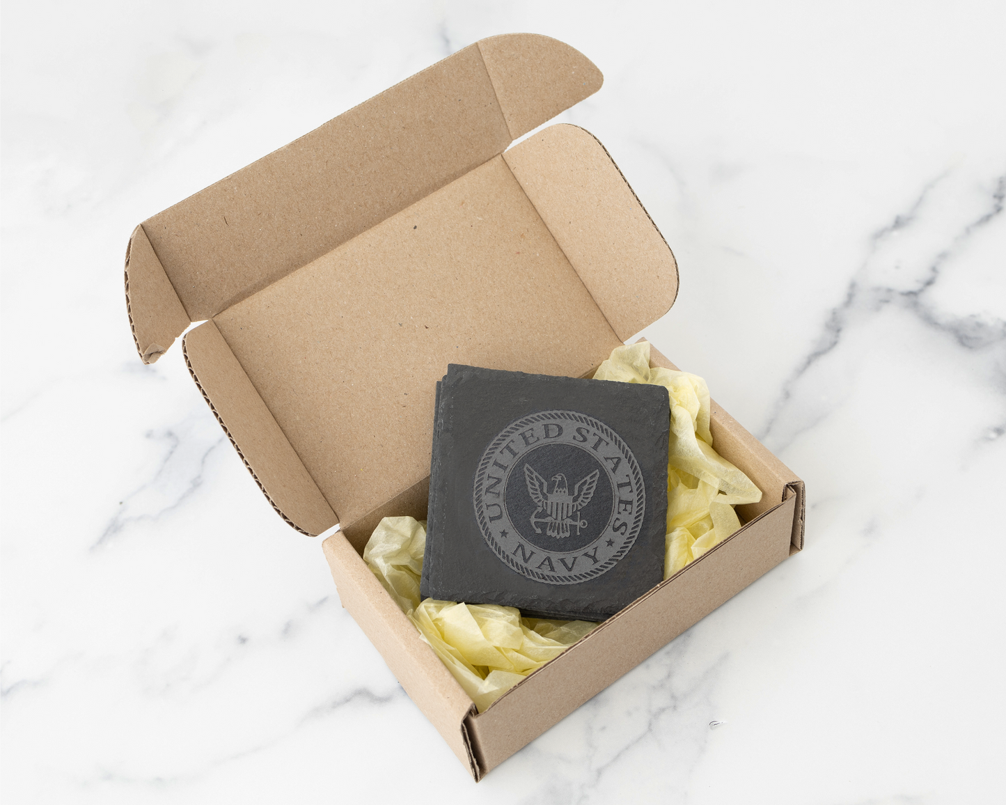 Navy emblem engraved coaster in a cardboard box on a marble surface