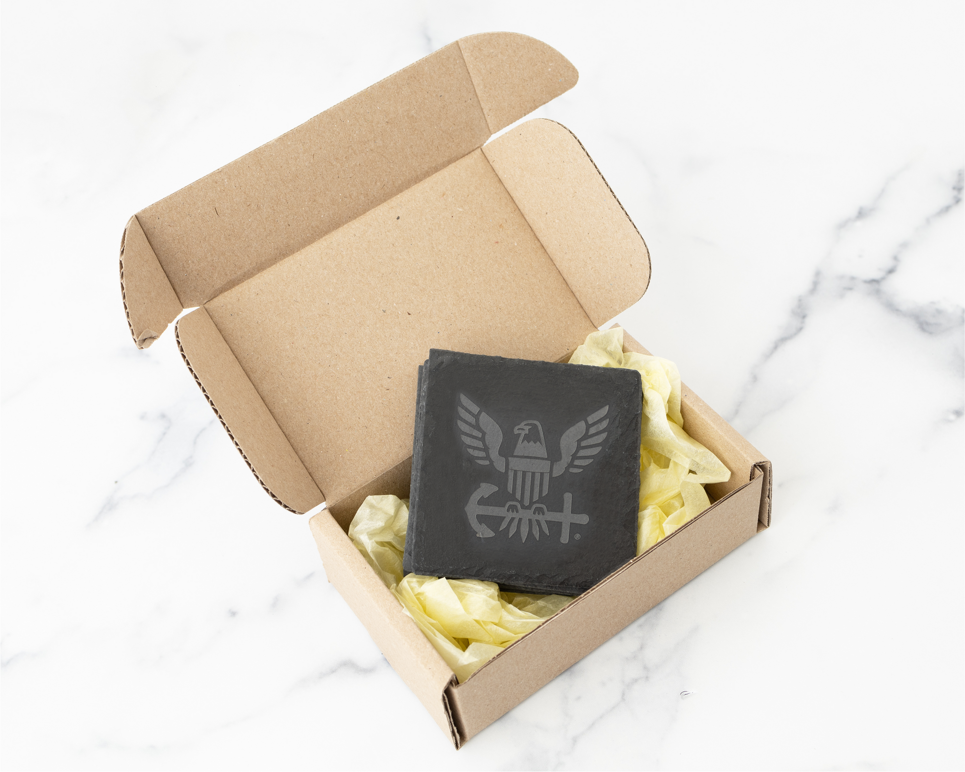 Open cardboard box with laser engraved slate coasters on a marble surface
