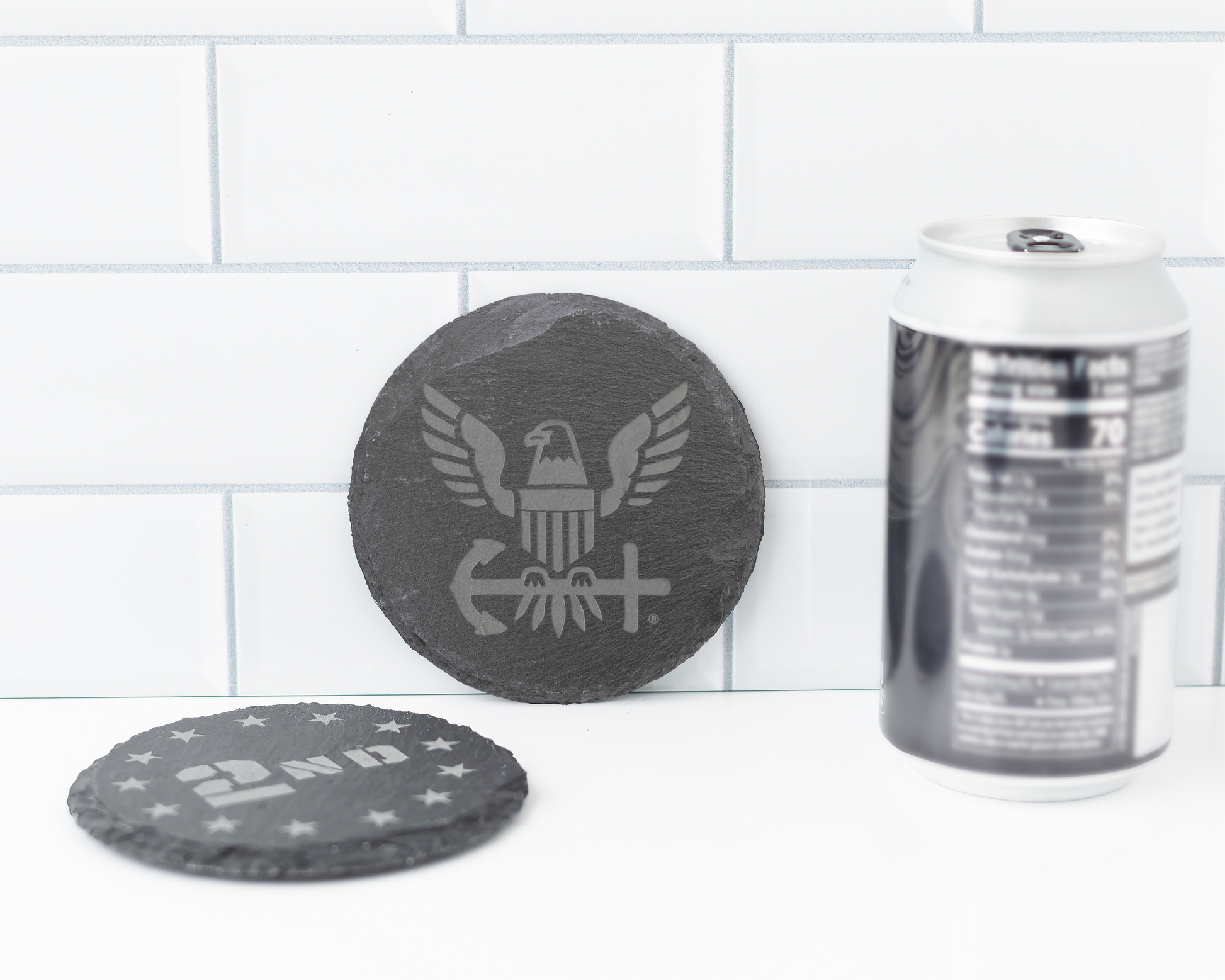 Two slate coasters with engraved designs on a tiled surface