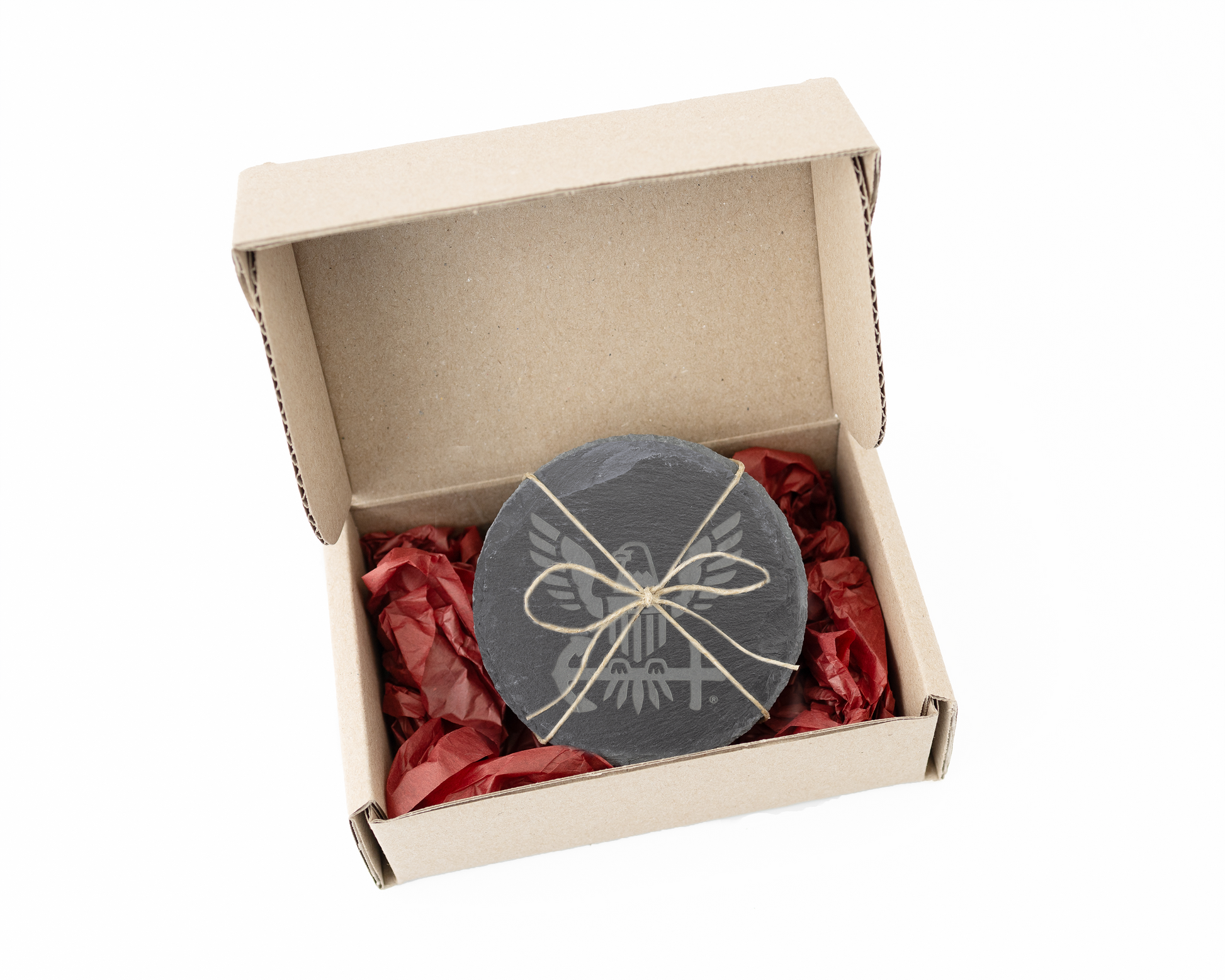 Round slate coasters with a bow design in an open cardboard box with red tissue paper.