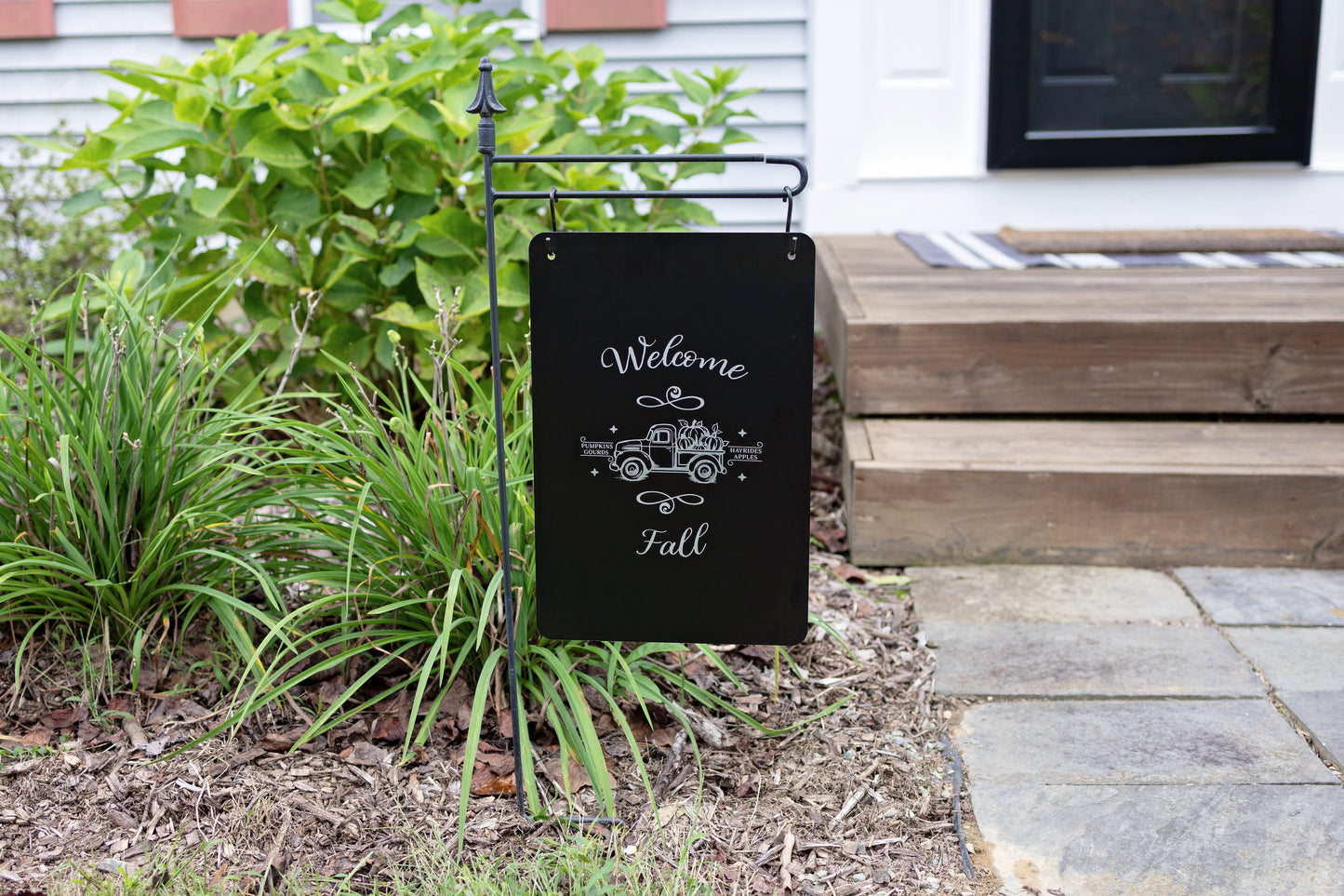 Garden sign with 'Welcome Fall' text and truck design on a garden flag stand outdoors.