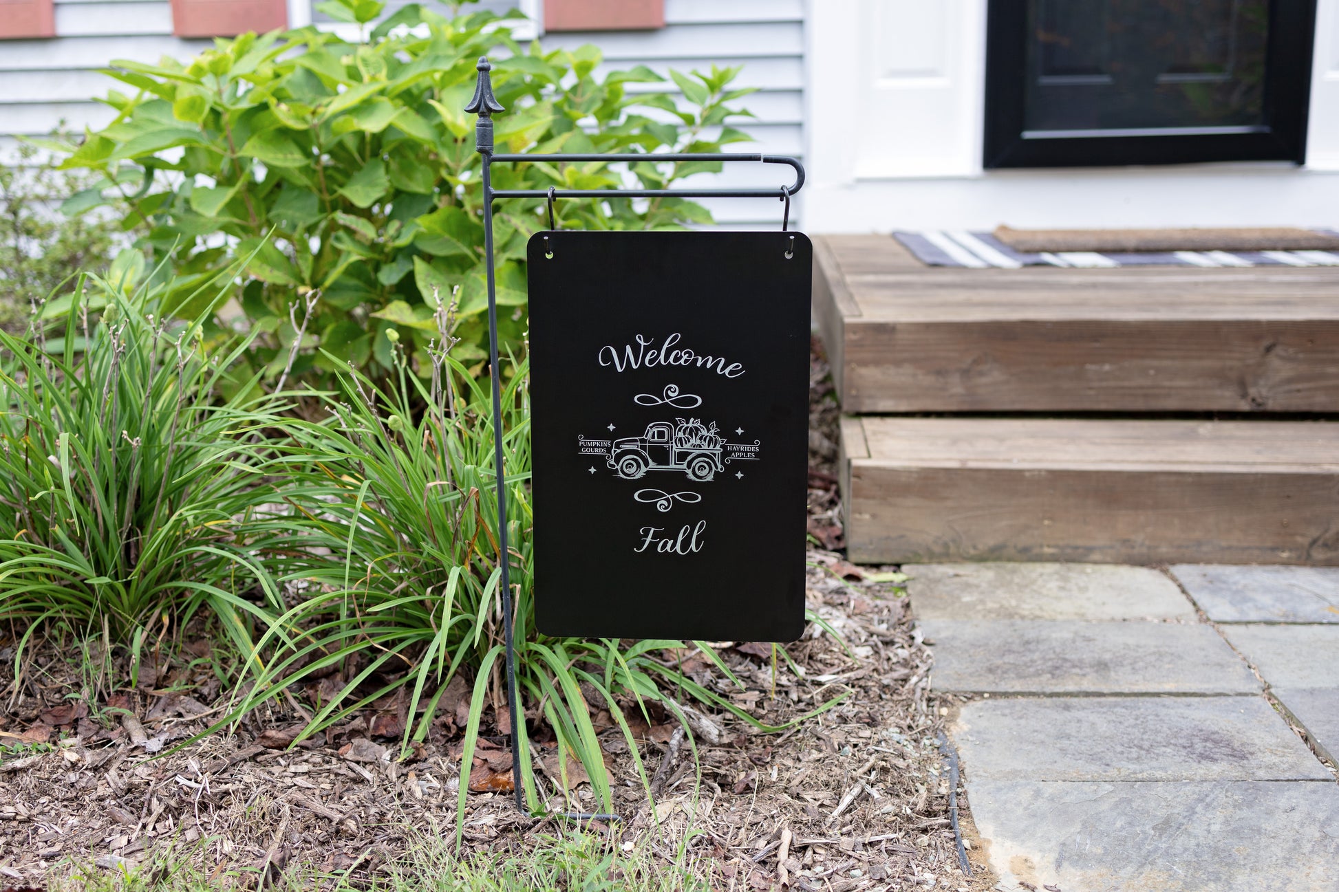 Garden sign with 'Welcome Fall' text and truck design on a garden flag stand outdoors.