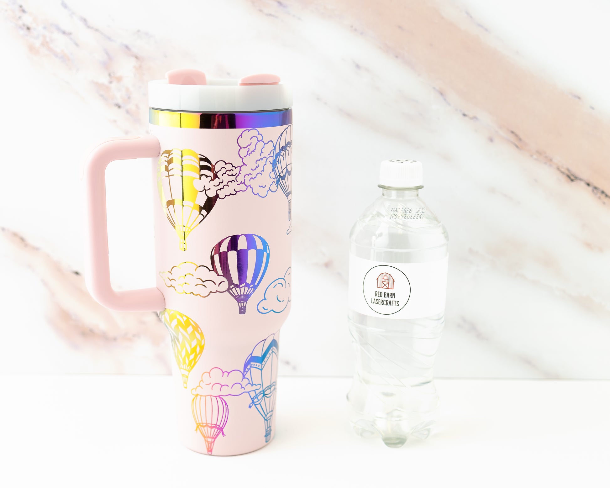 Laser engraved pink and rainbow 40oz stainless steel tumbler with hot air balloon and cloud design. Shown with a water bottle for size comparison.
