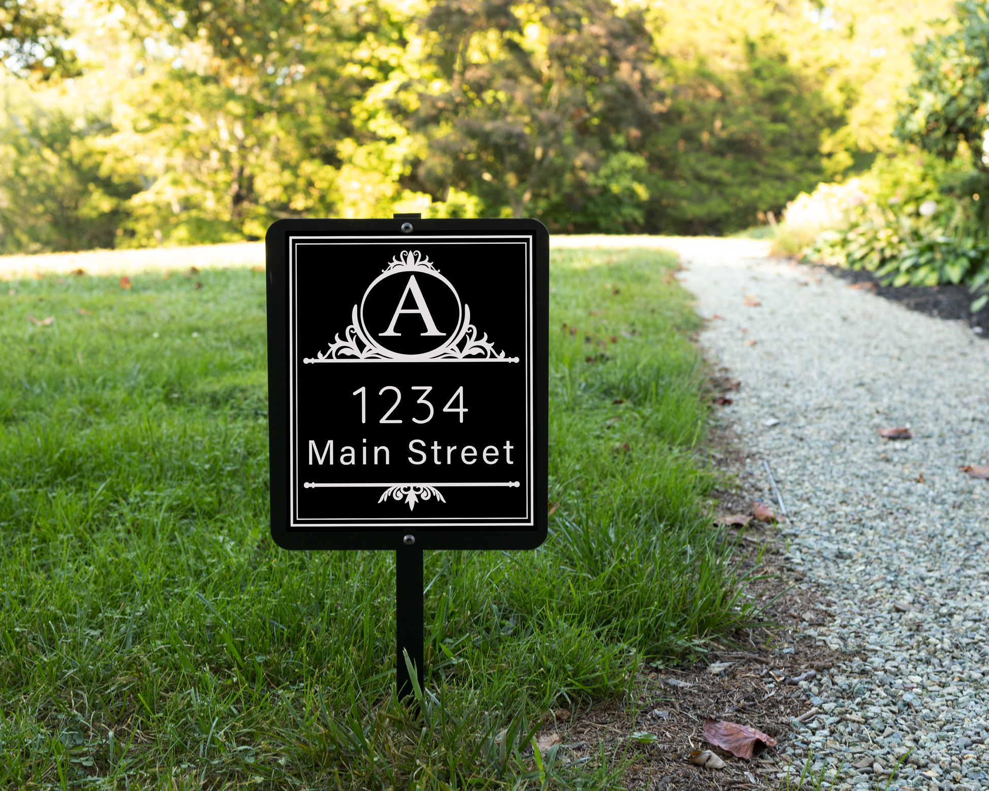 Black garden sign engraved with a decorative monogram and an address. Shown on a grassy lawn.