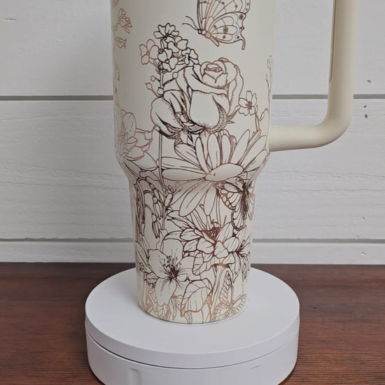 Cream and copper tumbler with floral and butterfly design on a white shiplap background